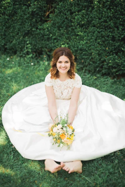 Belle mariée assise sur le sol tenant un bouquet souriant à la caméra — Photo