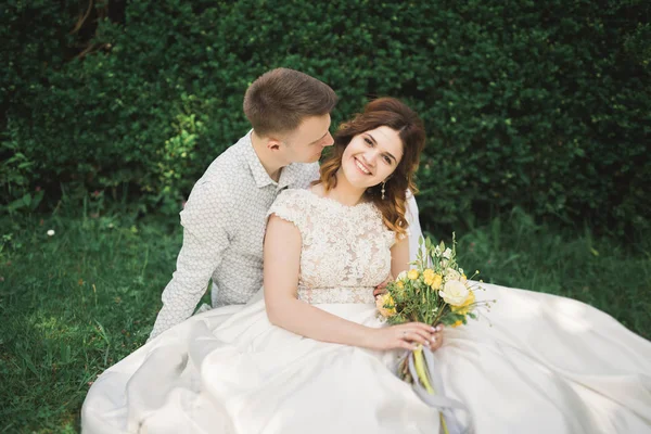Pasangan pengantin baru yang bahagia berjalan di taman pada hari pernikahan mereka dengan karangan bunga — Stok Foto