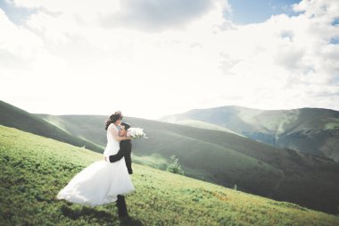 Yeni evli çift, gelin ve damat öpüşüyor, mükemmel dağ manzarasında sarılıyorlar, mavi gökyüzü