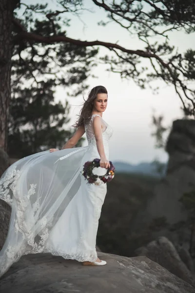 Magnifique mariée en robe élégante tenant bouquet posant près de la forêt — Photo