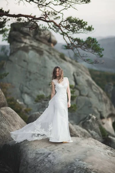 Gorgeous bride in elegant dress holding bouquet posing near forest