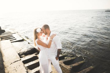 Düğün çifti mavi denizin yanındaki kayalarda öpüşüyor ve sarılıyor.