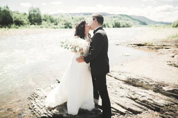 Красива весільна пара цілується і обіймається біля берега гірської річки з камінням — стокове фото