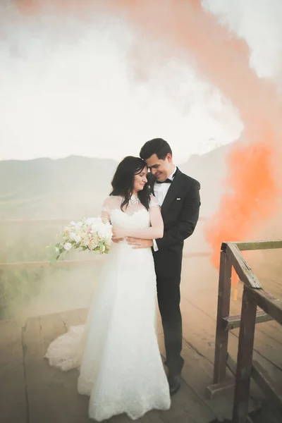 Свадебная пара позирует рядом со скалами с цветным дымом позади них — стоковое фото