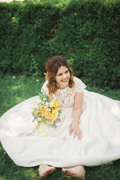 Sposa. Bella giovane donna bionda nel parco con corona di fiori e bouquet in una calda giornata estiva — Foto Stock