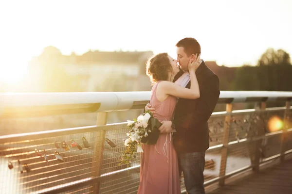 Casal de amor elegante, noivo, noiva com vestido rosa beijando e abraçando em uma ponte ao pôr do sol — Fotografia de Stock