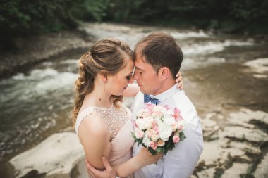 Mutlu çift düğün sarılma ve birbirlerine arka plan gölde gülümseyen orman