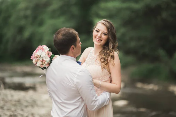 Elegan bergaya lembut pengantin pria dan pengantin wanita dekat sungai dengan batu. Pernikahan pasangan jatuh cinta — Stok Foto