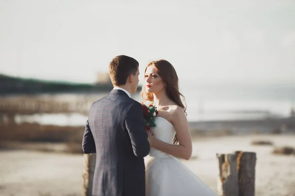 Ślub para, pan młody, panna młoda z bukiet pozowanie w pobliżu morza na zachód słońca — Zdjęcie stockowe