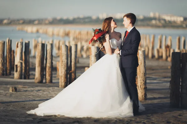 Beau jeune couple de mariage, mariée et marié posant près des poteaux en bois sur la mer de fond — Photo