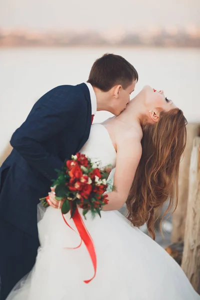 Mariage couple, marié, mariée avec bouquet posant près de la mer au coucher du soleil — Photo