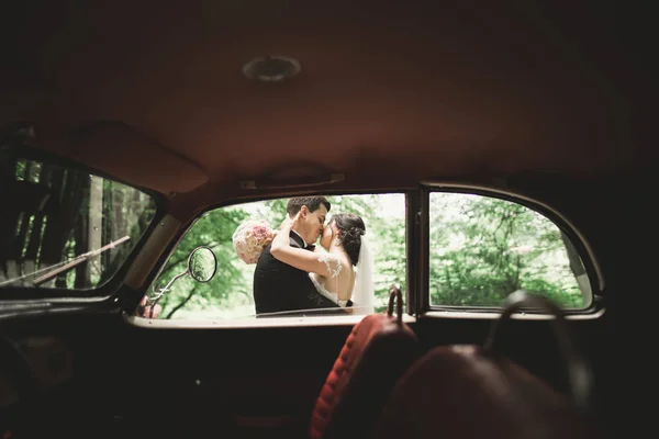 Happy newlywed couple, man and wife kissing near stylish retro car — Stock Photo, Image
