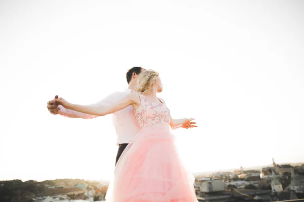 Jong koppel in liefde poseren op dak met uitzicht op de perfecte stad hand in hand en knuffelen. Prachtige zonsondergang — Stockfoto