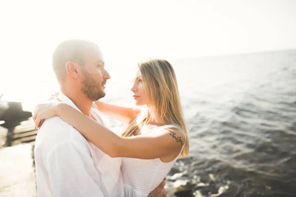 在蓝色大海边的岩石上亲吻拥抱的新婚夫妇 — 图库照片
