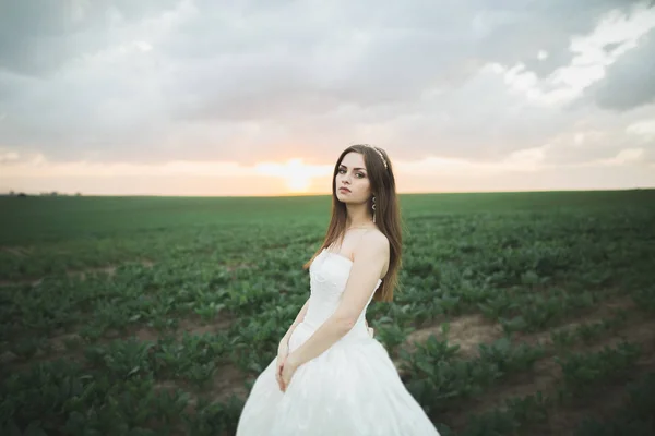 Красивая брюнетка невеста в элегантном белом платье держа букет, позируя аккуратные деревья — стоковое фото