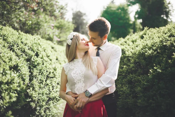 Молодая красивая пара целуется и обнимается возле деревьев с цветами в летнем парке — стоковое фото