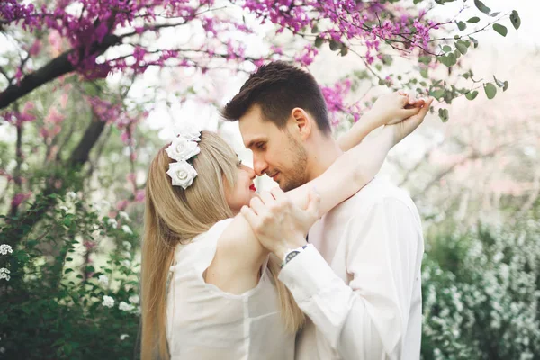 Joven hermosa pareja besándose y abrazándose cerca de los árboles con flor en el parque de verano —  Fotos de Stock