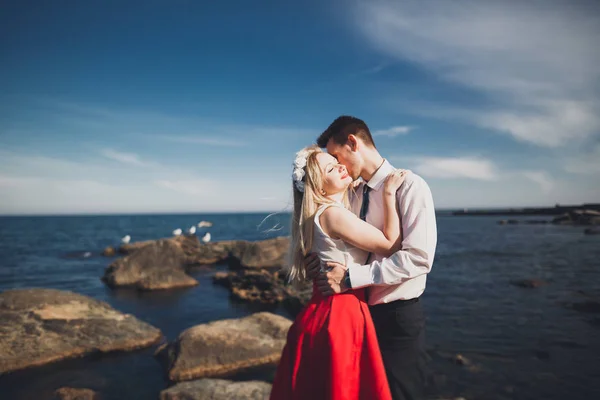 Casal amoroso romântico posando em pedras perto do mar, céu azul — Fotografia de Stock