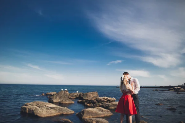 Romantica coppia amorevole posa su pietre vicino al mare, cielo blu — Foto Stock