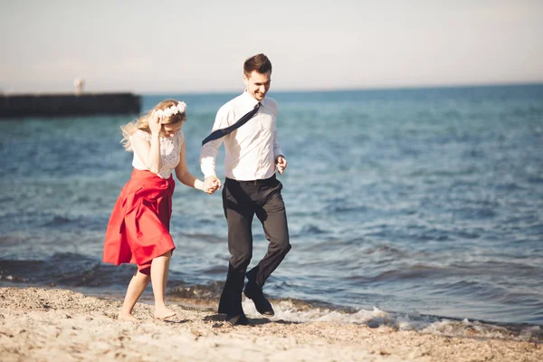 Νεαρό ζευγάρι χαρούμενος περπάτημα στην παραλία χαμογελώντας εκμετάλλευση γύρω από το άλλο. Ιστορία αγάπης — Φωτογραφία Αρχείου