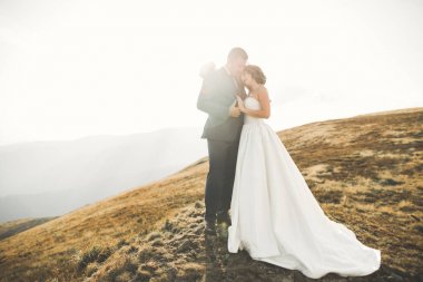 Yeni evli çift, gelin ve damat öpüşüyor, mükemmel dağ manzarasında sarılıyorlar, mavi gökyüzü