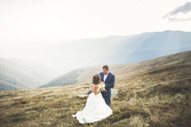 Yeni evli çift, gelin ve damat öpüşüyor, mükemmel dağ manzarasında sarılıyorlar, mavi gökyüzü