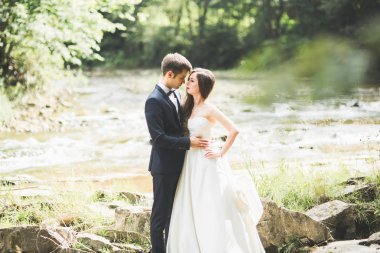 Zarif nazik şık damat ve gelin taşlarla Nehri yakınında. Evlilik çift aşık