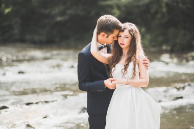 Şık şık mutlu esmer gelin ve dağlarda güzel bir nehir arka plan üzerinde muhteşem damat