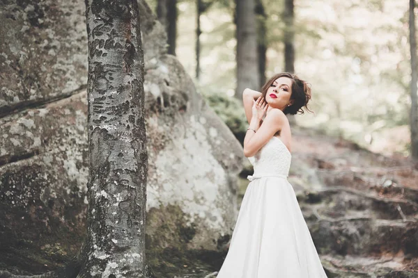 Hermosa novia con un ramo posando en el bosque con rocas. Al aire libre — Foto de Stock