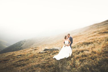 Yeni evli çift, gelin ve damat öpüşüyor, mükemmel dağ manzarasında sarılıyorlar, mavi gökyüzü