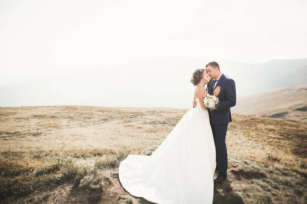 Jovem casal recém-casado, noiva e noivo beijando, abraçando na visão perfeita das montanhas, céu azul — Fotografia de Stock