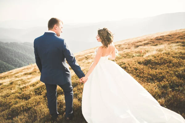 Hermosa pareja de boda posando en la cima de una montaña al atardecer —  Fotos de Stock