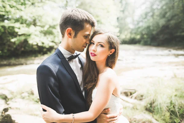 Elegante gentile sposo elegante e sposa vicino al fiume con pietre. Matrimonio coppia innamorata — Foto Stock