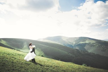 Yeni evli çift, gelin ve damat öpüşüyor, mükemmel dağ manzarasında sarılıyorlar, mavi gökyüzü