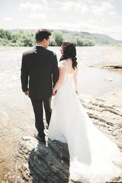 Elegante gentile sposo elegante e sposa vicino al fiume con pietre. Matrimonio coppia innamorata — Foto Stock