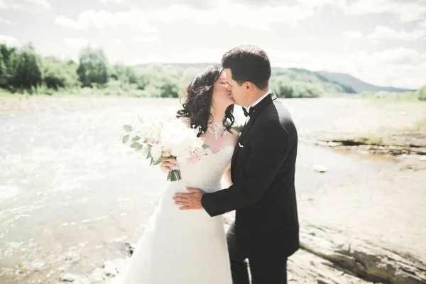 Gyönyörű esküvői pár csókolózik és ölelkezik a part közelében egy hegyi folyó kövekkel — Stock Fotó
