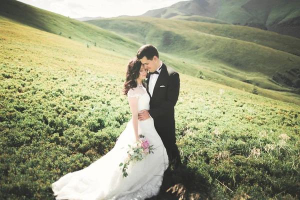 Yeni evli çift, gelin ve damat öpüşüyor, mükemmel dağ manzarasında sarılıyorlar, mavi gökyüzü