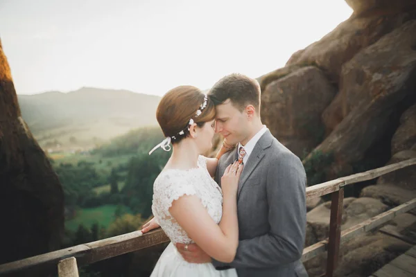 Young newly wed couple, bride and groom kissing, hugging on perfect view of mountains, blue sky — Stock Photo, Image