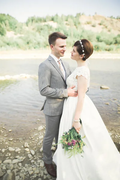 Casamento lindo casal beijando e abraçando perto da costa de um rio de montanha com pedras — Fotografia de Stock
