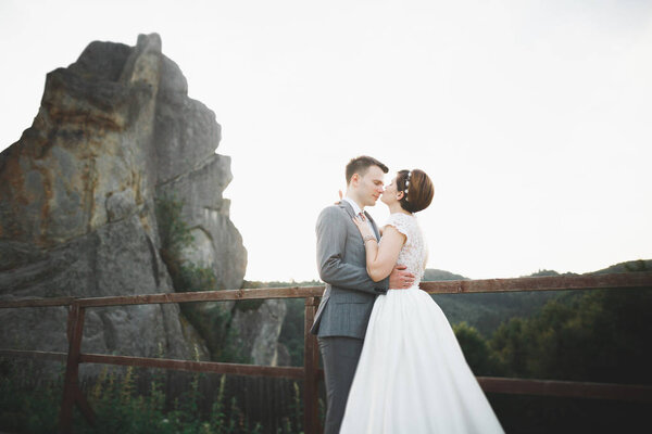 Gorgeous bride and stylish groom walking at sunny landscape, boho wedding couple, luxury ceremony at mountains with amazing view, space for text