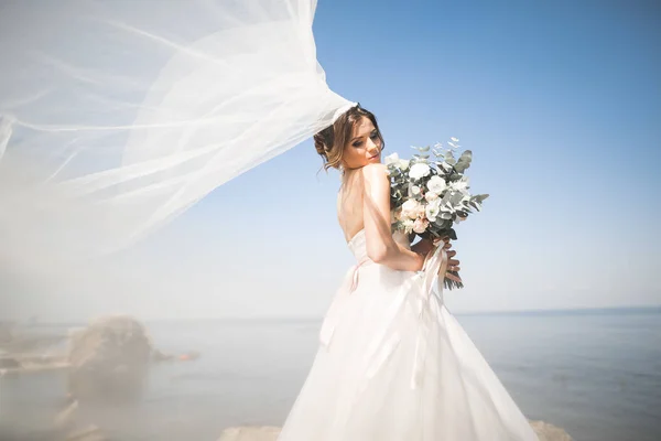 Bella giovane sposa con bouquet da sposa in posa sullo sfondo mare — Foto Stock