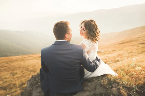 Hermosa pareja de boda posando en la cima de una montaña al atardecer —  Fotos de Stock