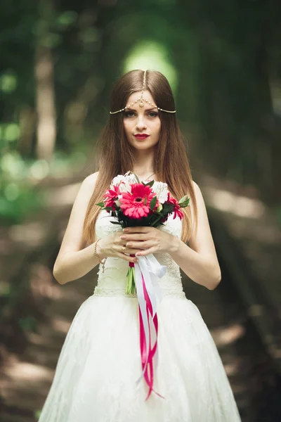 Sposa. Bella giovane donna bionda nel parco con corona di fiori e bouquet in una calda giornata estiva — Foto Stock