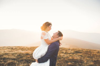 Güzel bir düğün çifti mükemmel bir manzarayla dağda öpüşüyor ve sarılıyor.