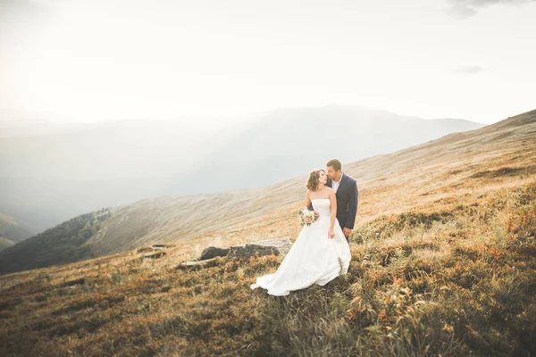 Krásné svatební pár pózuje na vrcholu hory při západu slunce — Stock fotografie