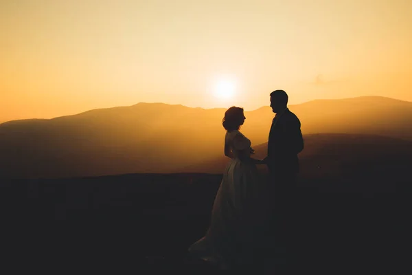 Красивая свадебная пара позирует на вершине горы на закате — стоковое фото