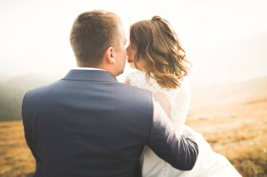 Yeni evli çift, gelin ve damat öpüşüyor, mükemmel dağ manzarasında sarılıyorlar, mavi gökyüzü