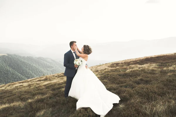 Yeni evli çift, gelin ve damat öpüşüyor, mükemmel dağ manzarasında sarılıyorlar, mavi gökyüzü