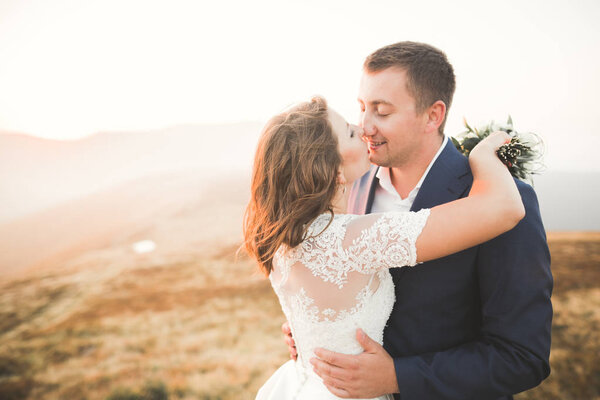 Beautiful wedding couple posing on top of a mountain at sunset