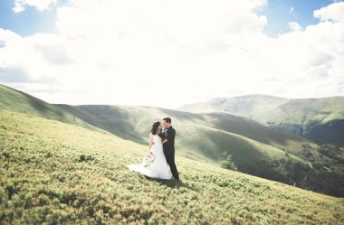 Yeni evli çift, gelin ve damat öpüşüyor, mükemmel dağ manzarasında sarılıyorlar, mavi gökyüzü